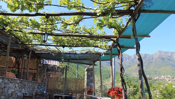An outdoor seating area with stone walls, wooden furniture, and a view of mountains. - Casa Scola Agriturismo (Gragnano)