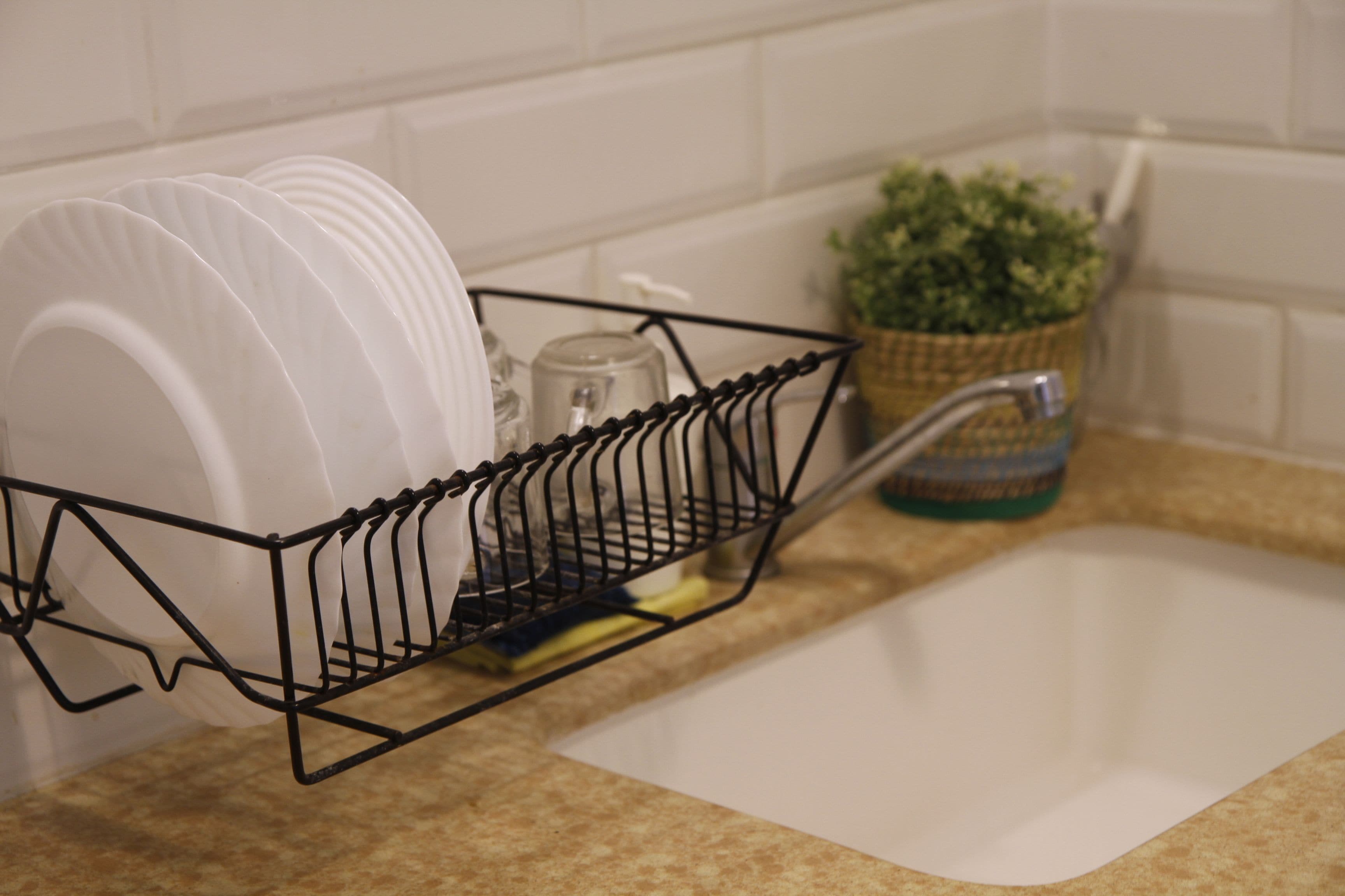 Un lavamanos de cocina con un escurreplatos que contiene platos blancos y una planta en maceta.