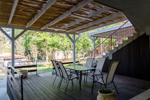 Um pátio externo com mesa e cadeiras, uma escadaria e vista para o verde ao redor.