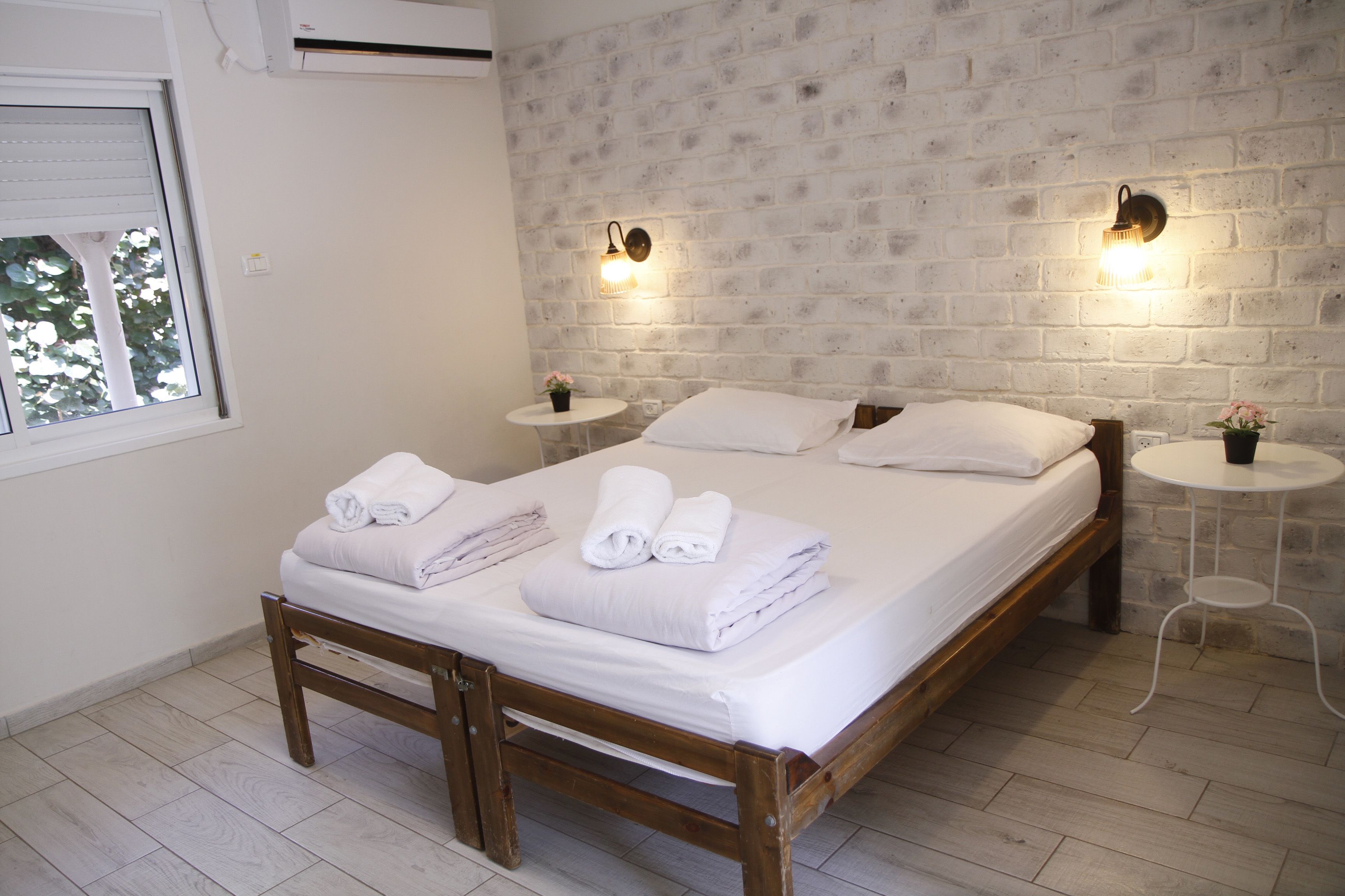 Una camera da letto con un letto in legno, lenzuola bianche, due comodini con lampade e un muro in mattoni.