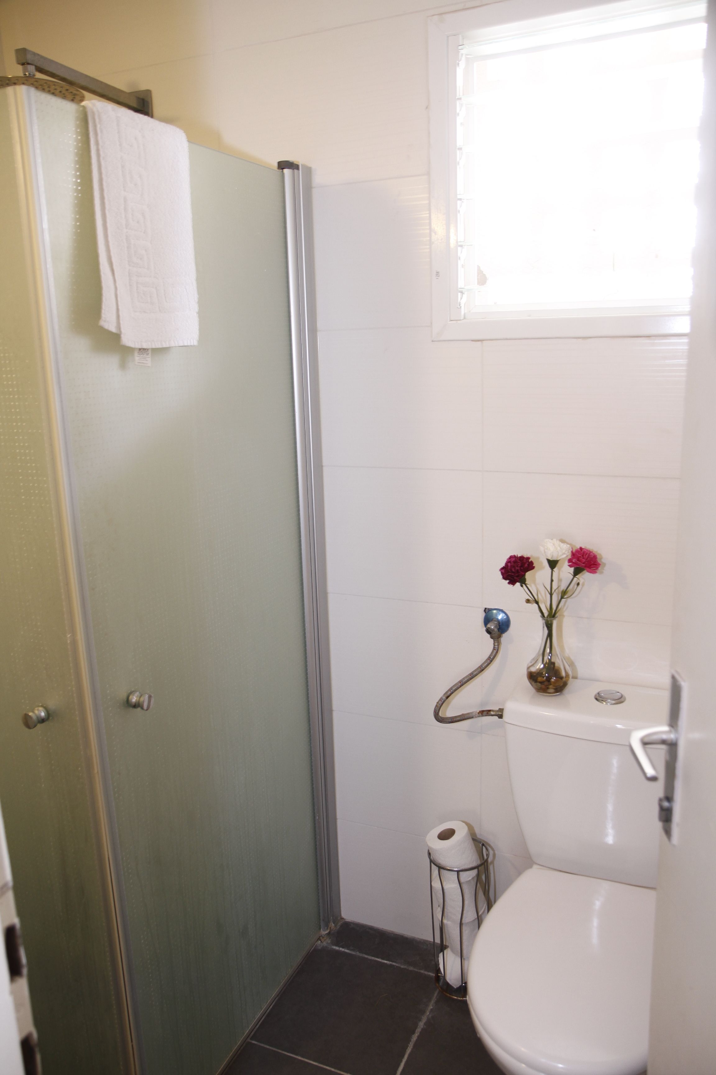 A bathroom with a glass shower door, a toilet, and a small window.
