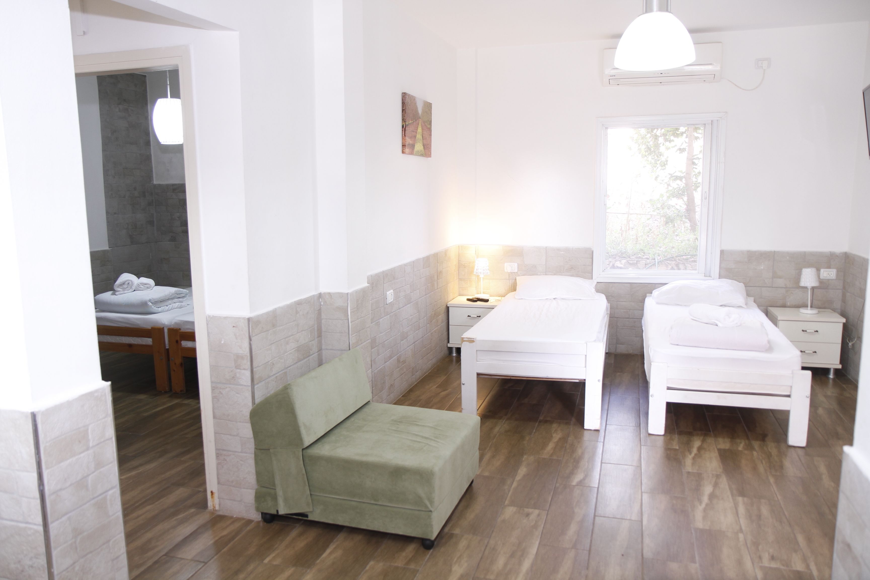A room with two beds, a green chair, a bedside table with a lamp, and a window.