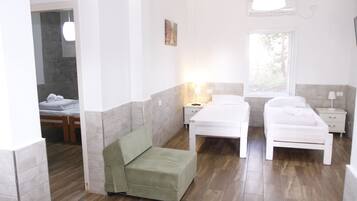 A room with two beds, a green chair, a bedside table with a lamp, and a window.