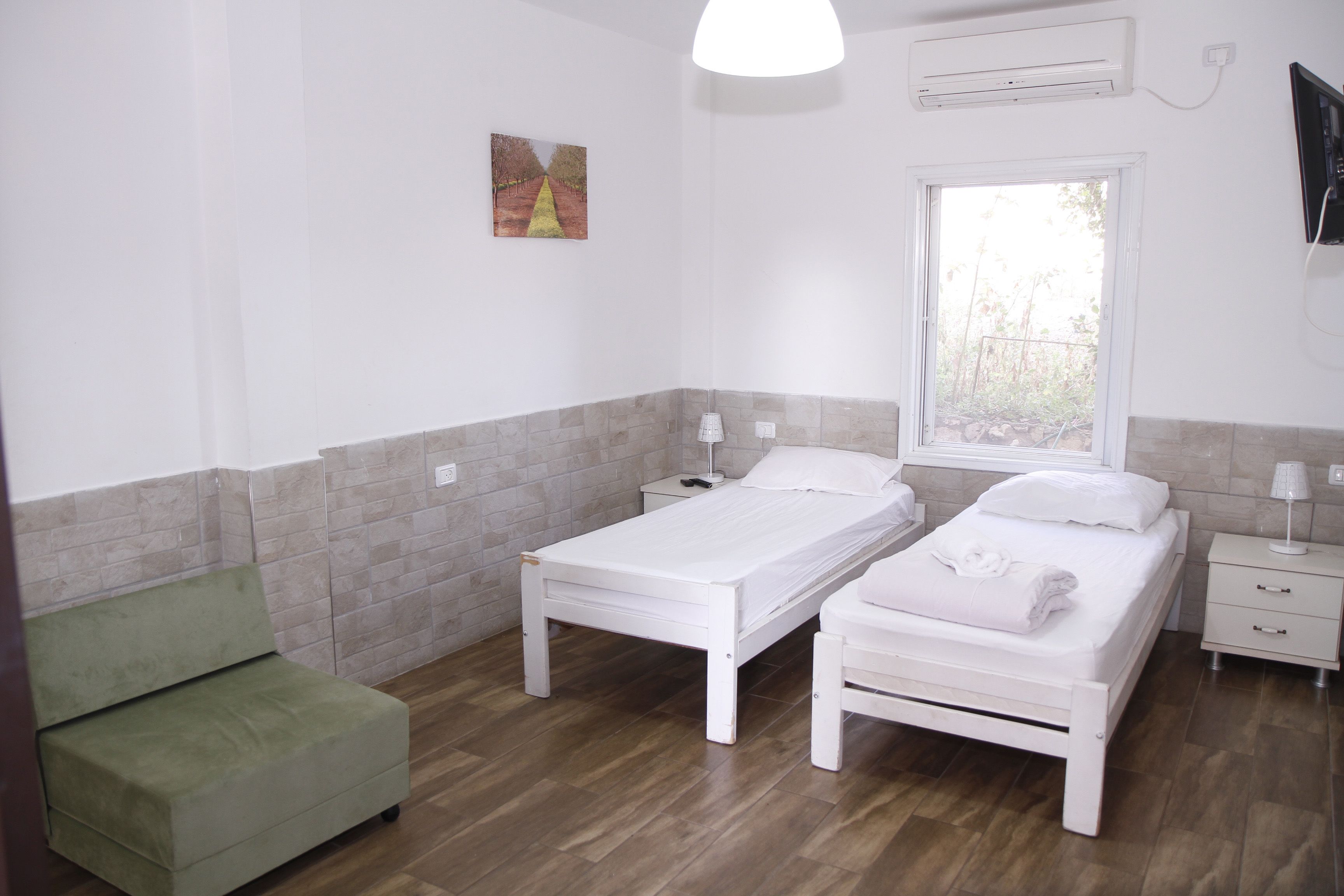 A bedroom with two single beds, a green sofa, a window, and a painting on the wall.