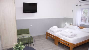 Ein Hotelzimmer mit Bett, einem an der Wand befestigten Fernseher, einem kleinen Tisch mit Pflanze und einem mit Vorhängen versehenen Fenster.