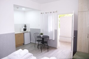 Quarto compacto com cozinha compacta, área de refeições com duas cadeiras, uma mesa pequena e uma cama.