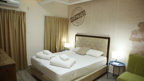 A hotel room with a large bed, two bedside tables, a green armchair, and a wall-mounted air conditioning unit. - Beit Alfa Kibbutz Country Lodging (Gilboa)