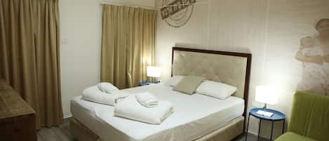 Habitación de hotel con una cama grande, dos mesitas de noche, un sillón verde y un aire acondicionado instalado en la pared.
