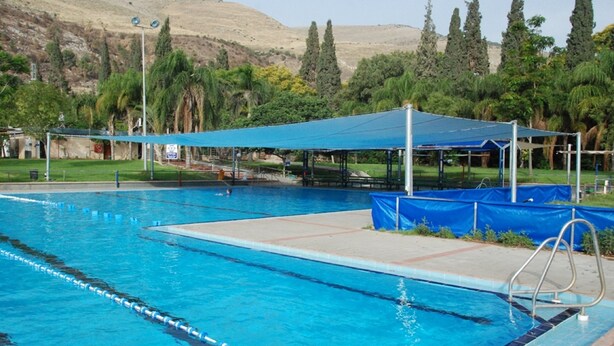 A swimming pool with a blue canopy, surrounded by trees and a hilly landscape. - Beit Alfa Kibbutz Country Lodging (Gilboa)