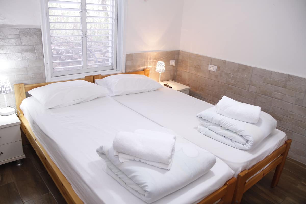 A neatly made bed with white linens and towels, a bedside table with a lamp, and a window with blinds.