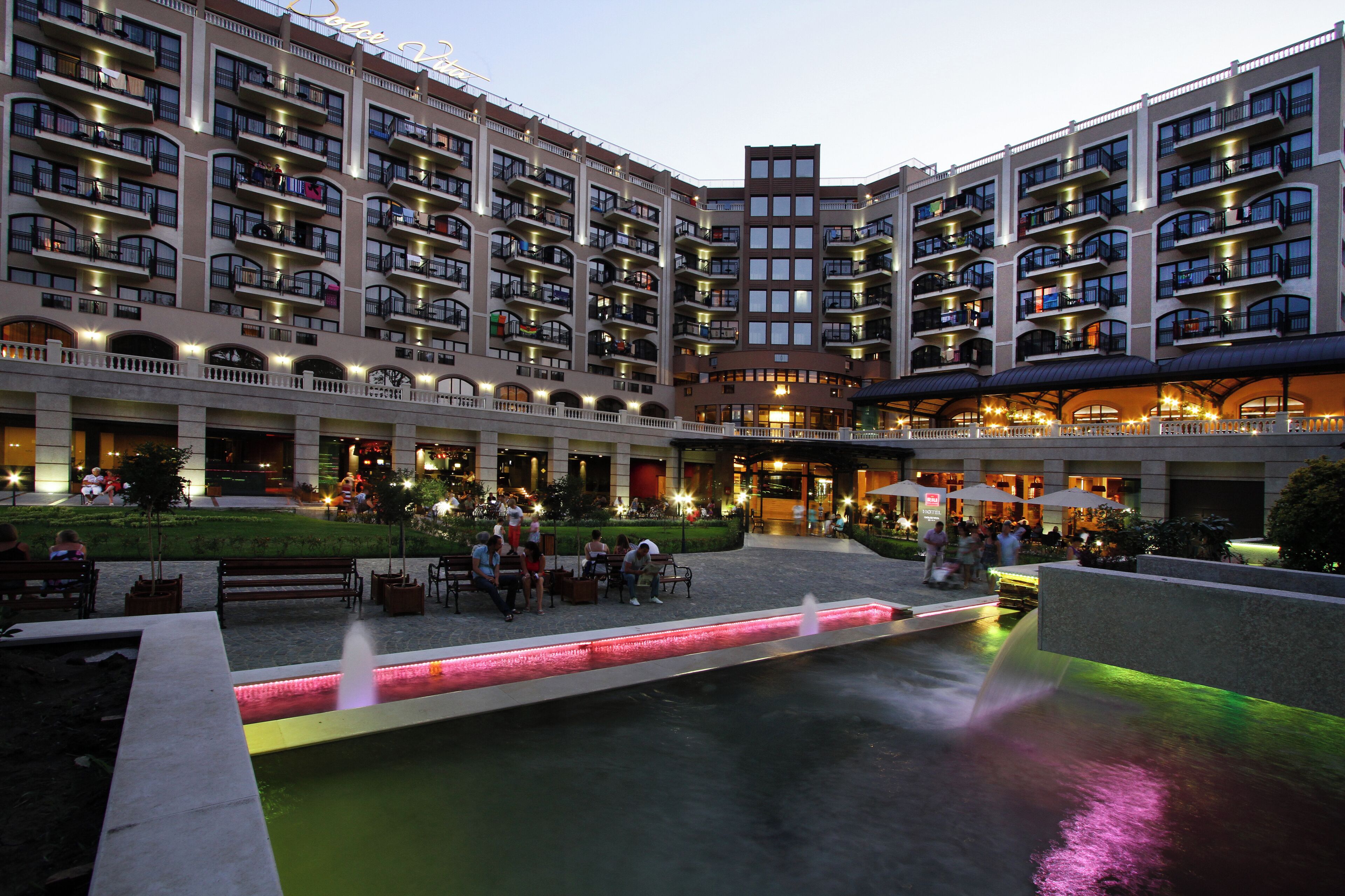 A hotel courtyard with multiple balconies, outdoor seating, and a water feature.