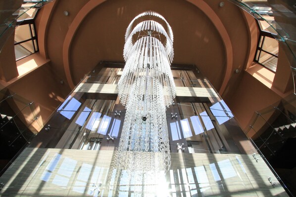 A large, ornate chandelier in a spacious atrium with high ceilings and large windows allowing natural light to enter.