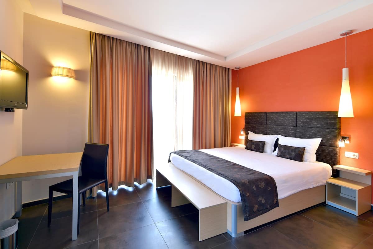 A hotel room with a bed, bedside tables, a desk, a chair, and a TV.