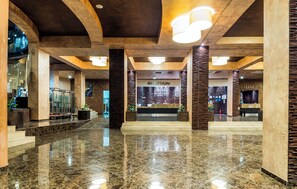 A spacious lobby with a polished marble floor, a reception desk, and a staircase leading to upper levels.