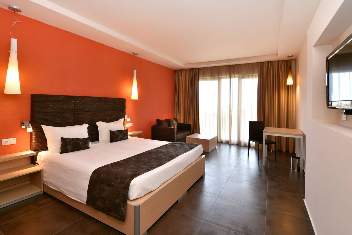 A modern hotel room with a large bed, a desk, and a TV.