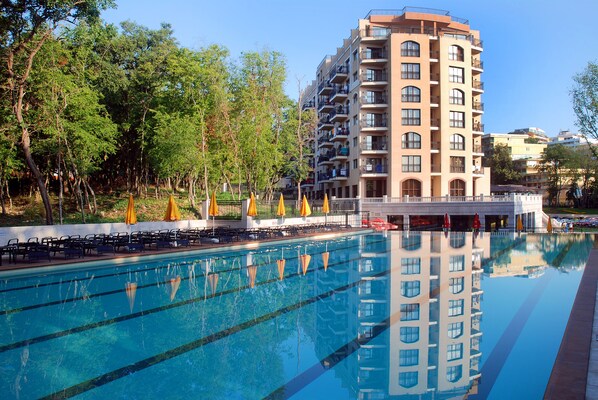 A hotel with a swimming pool, outdoor seating, and a reflection of the building in the water.