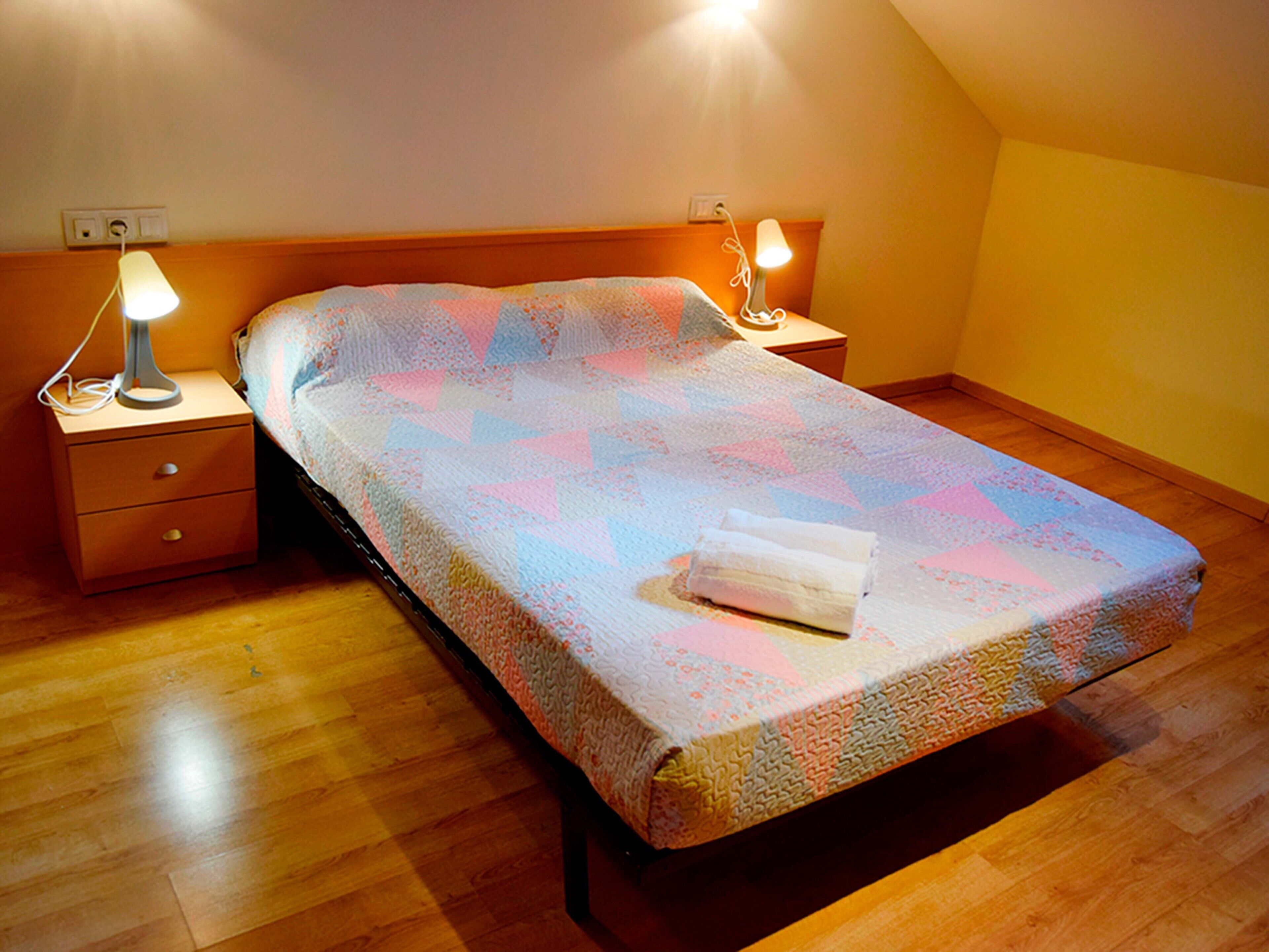 A single bed in a room with wooden flooring, two bedside tables, and a wall socket.