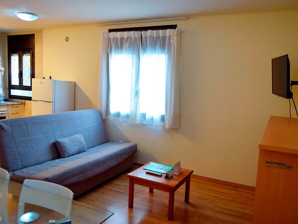 Un espacio habitable compacto con sofá, una mesita, televisor y ventana con cortinas.