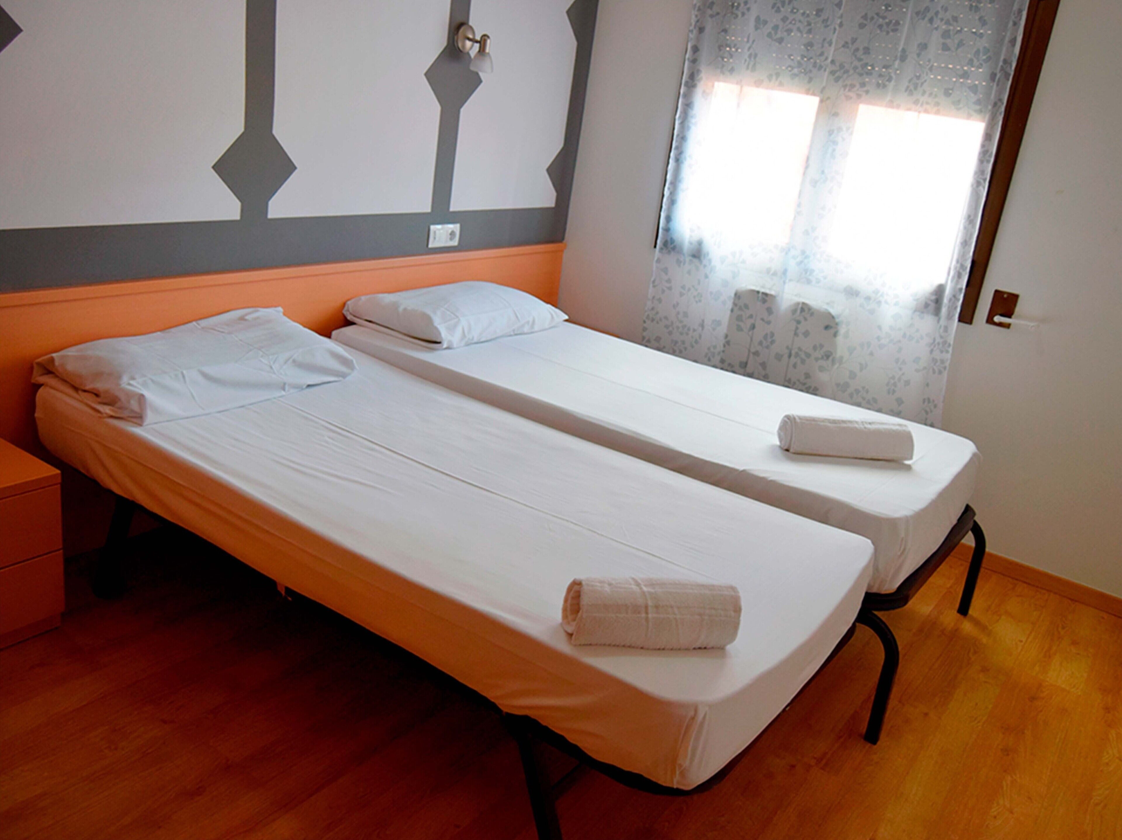 A double bed room with two single beds, a nightstand, and a window with floral curtains.