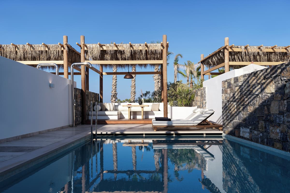 A pool area with a lounge chair, a small table, and a thatched roof structure.