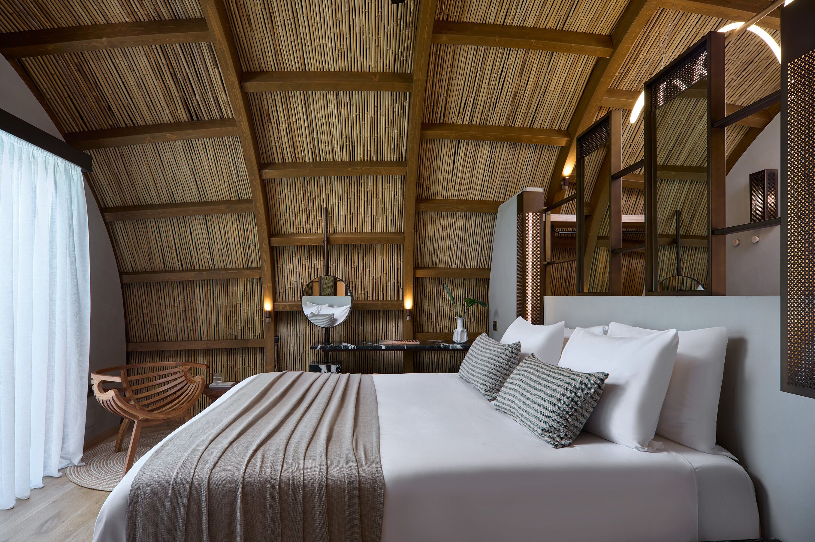 Ein Schlafzimmer mit einem großen Bett, einer Holzbalkendecke, einem Nachttisch mit Lampe und einem Sessel.