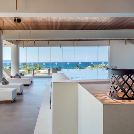 A modern lounge area with a pool, large windows offering a view of the sea, and a wooden ceiling.