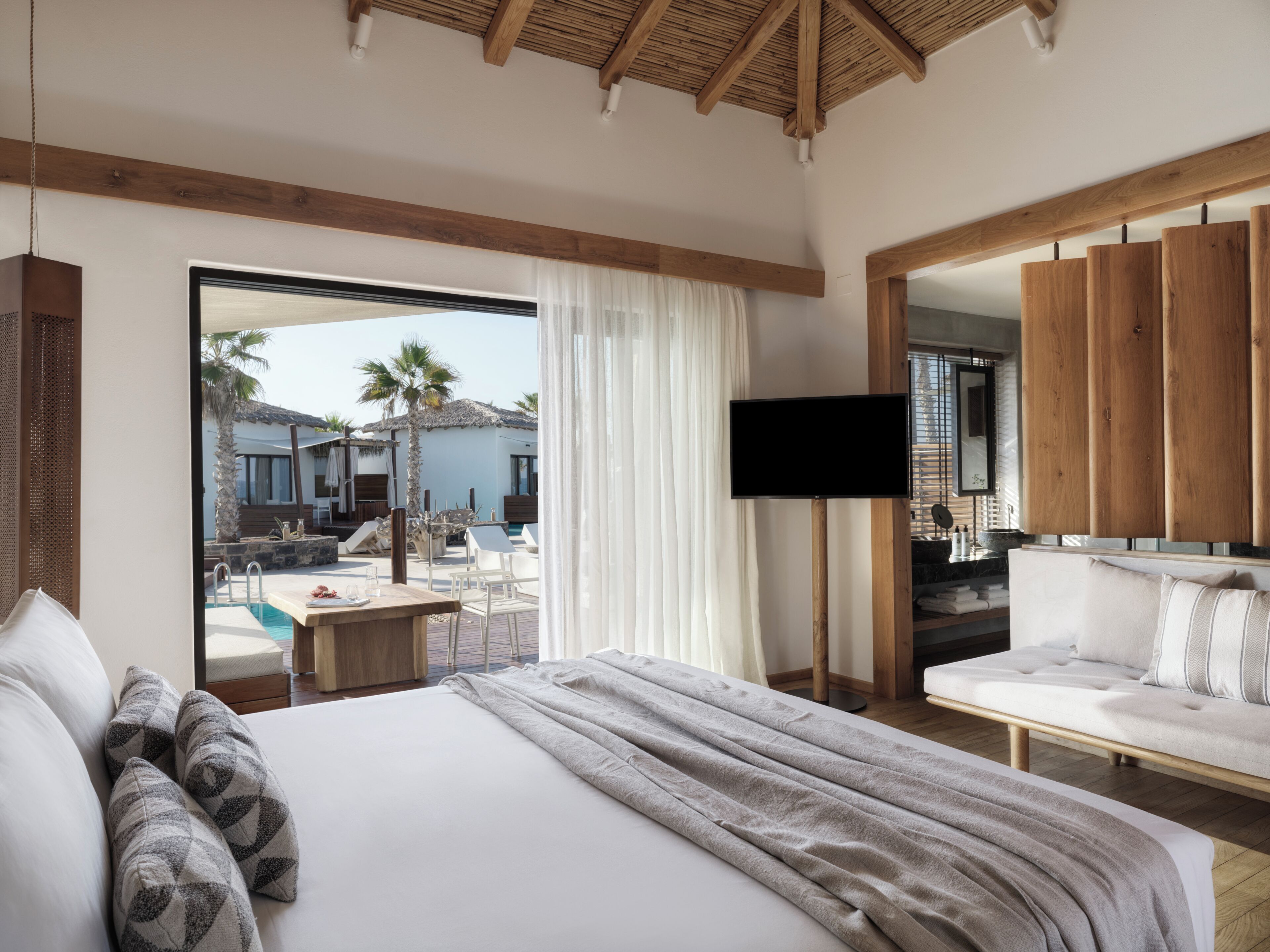 Ein Hotelzimmer mit Bett, Fernseher, Sofa und Blick auf einen Außenpool.