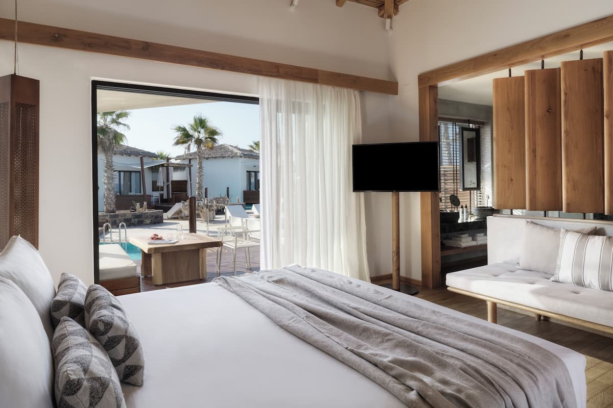 A hotel room with a bed, a TV, a sofa, and a view of an outdoor pool area.