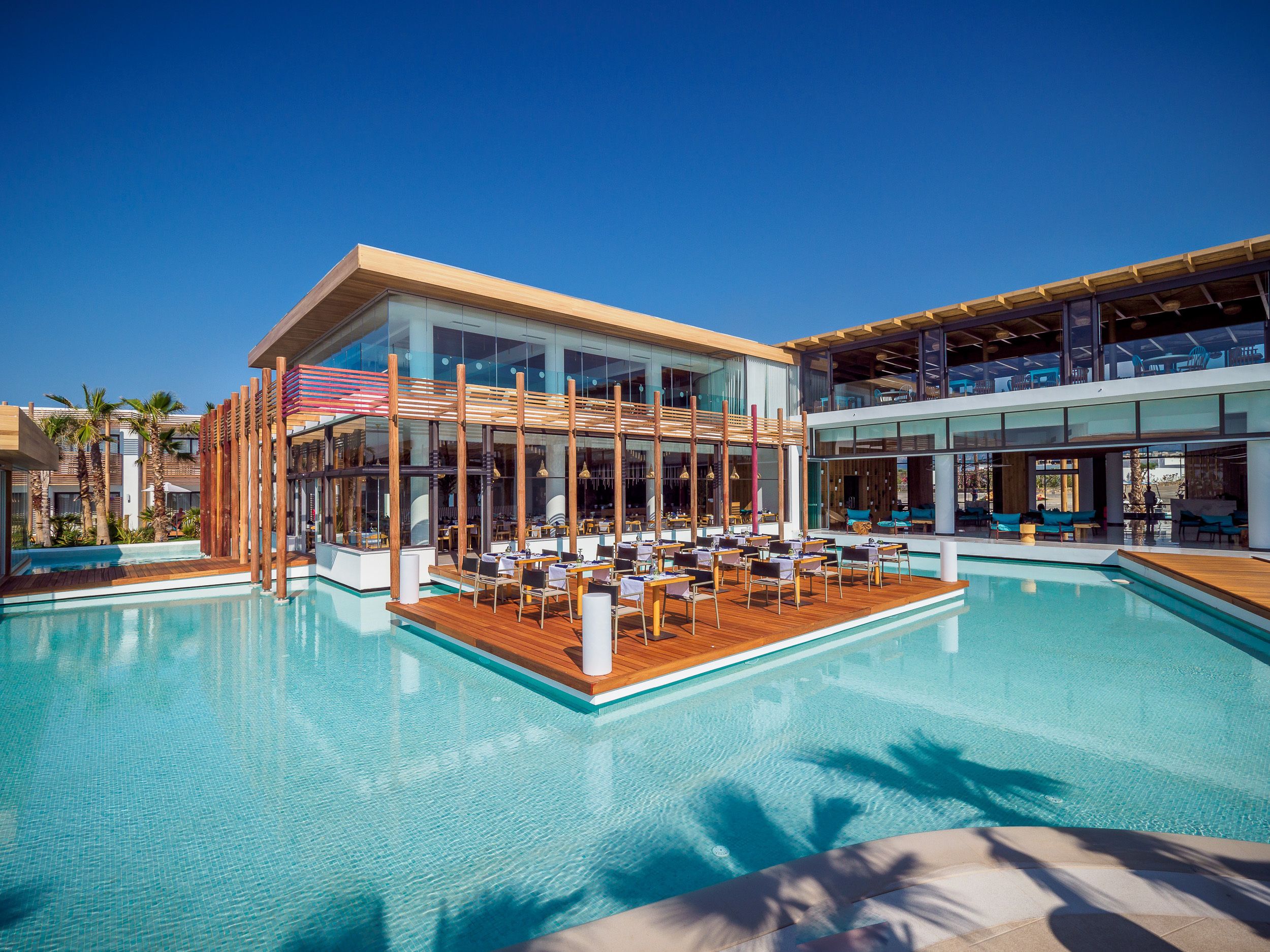 A modern hotel with a pool area, outdoor seating, and a view of the ocean.