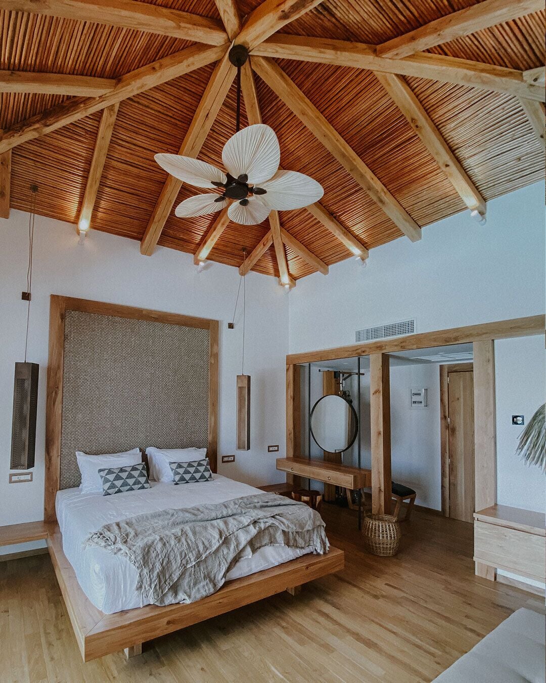 Ein geräumiges Schlafzimmer mit einem großen Bett, Holzbalken, einem Deckenventilator und einem Holzschrank.