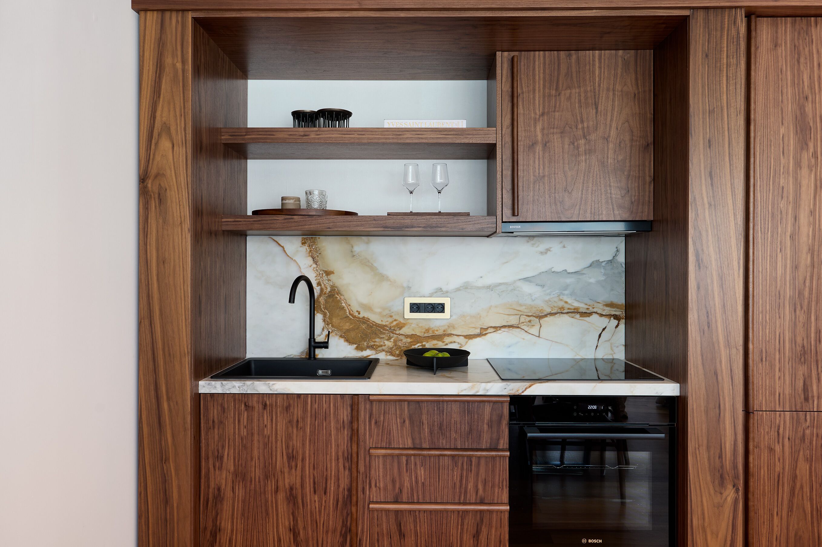 Una cocina con armarios de madera, salpicadero de mármol, un lavamanos negro y lavavajillas Bosch.