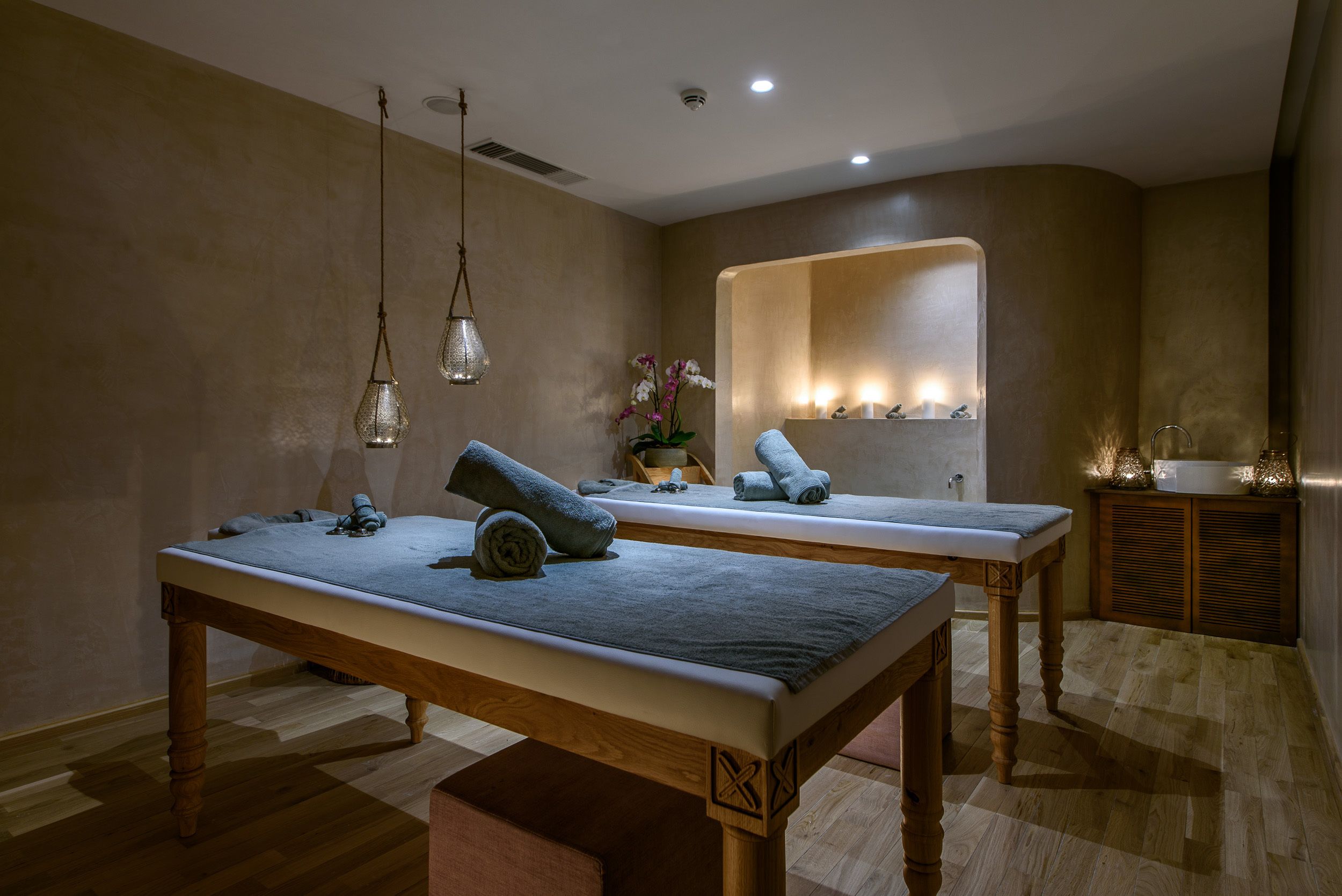 Un cuarto de spa con dos camillas de madera, un espejo y un pequeño armario con velas.