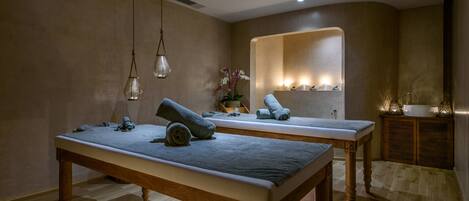 Un cuarto de spa con dos camillas de madera, un espejo y un pequeño armario con velas.