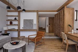 A modern living room with a sofa, a wooden chair, a small round table with fruit, and a bookshelf.