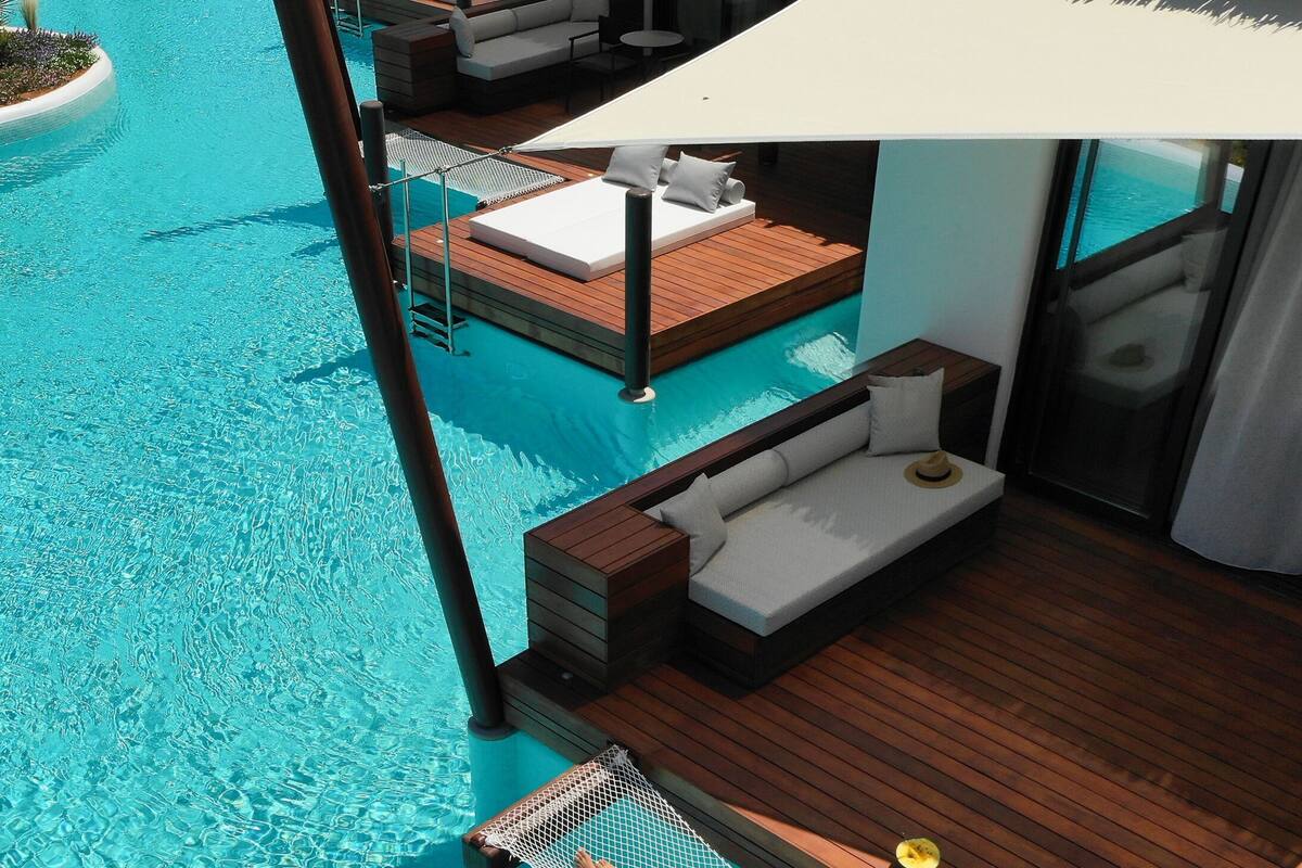 A resort pool area with wooden deck loungers, thatched umbrellas, and a clear blue pool.