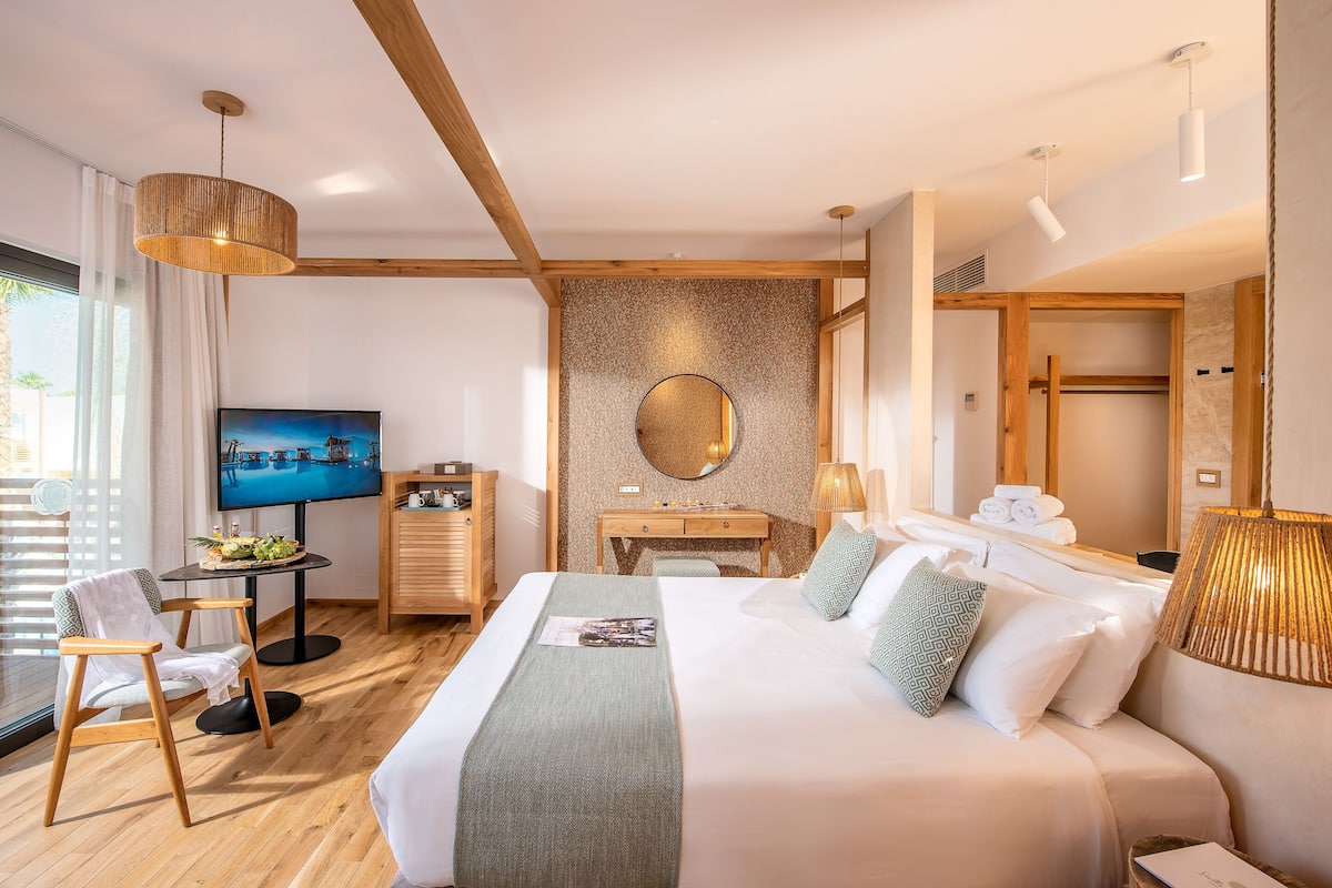 A modern hotel room with a large bed, a desk, a television, and a view of the outdoors.
