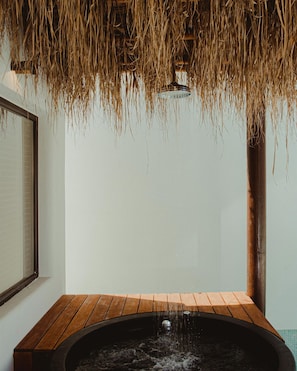 A wooden bathtub with water flowing into it, set against a white wall with a window and a wooden beam overhead.