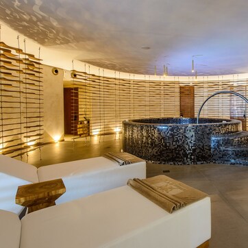 A modern spa with a central mosaic hot tub, wooden slats on the walls, and a minimalist design.