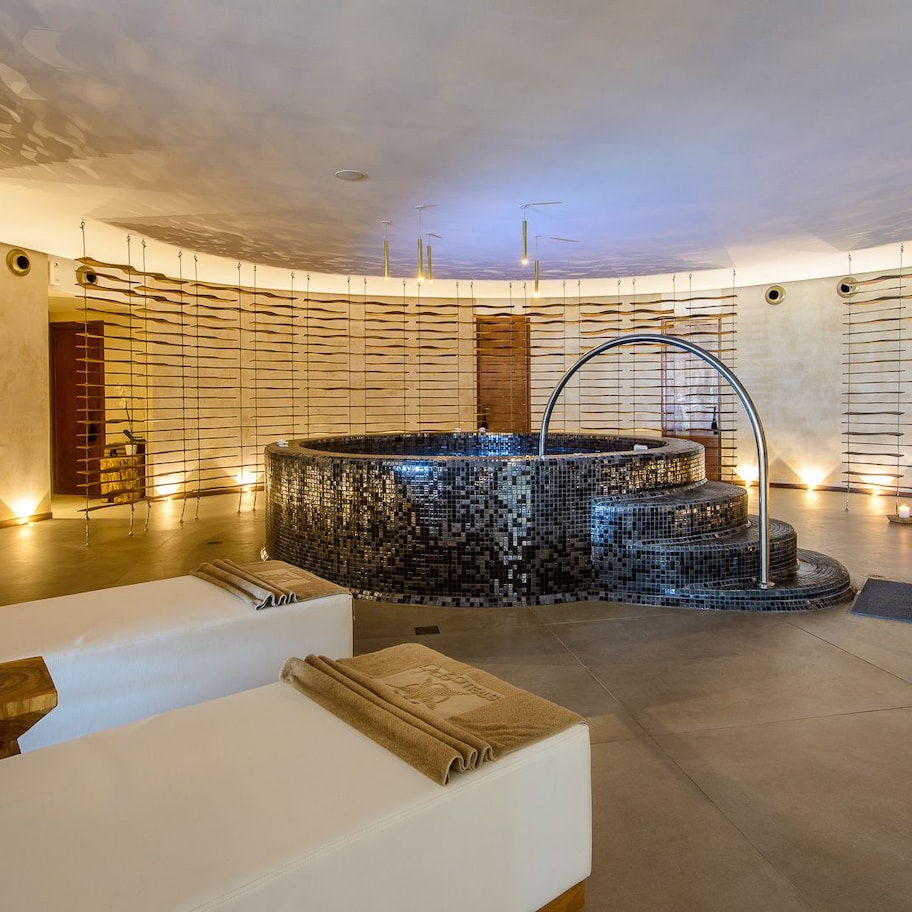 A modern spa with a central mosaic hot tub, wooden slats on the walls, and a minimalist design.