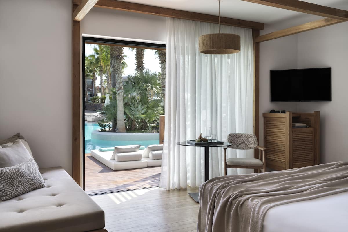 A modern hotel room with a large bed, a sofa, a small table, and a TV.