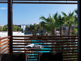 A poolside view with wooden railings, a table with a book and sunglasses, and palm trees.