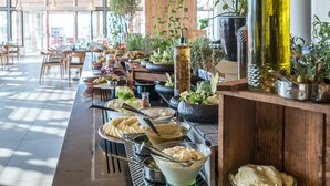 A modern restaurant interior with a long counter, hanging pendant lights, and various plants.