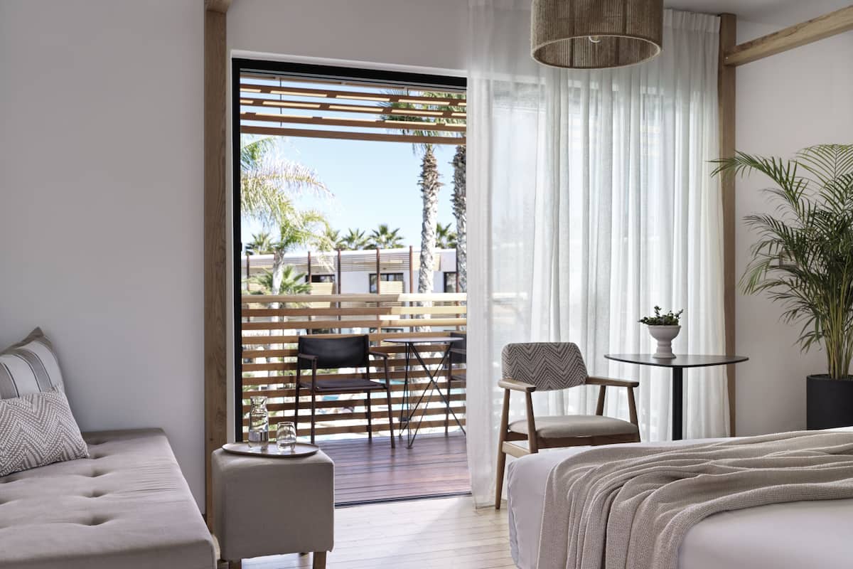A modern hotel room with a balcony, a bed, a sofa, and a dining area.