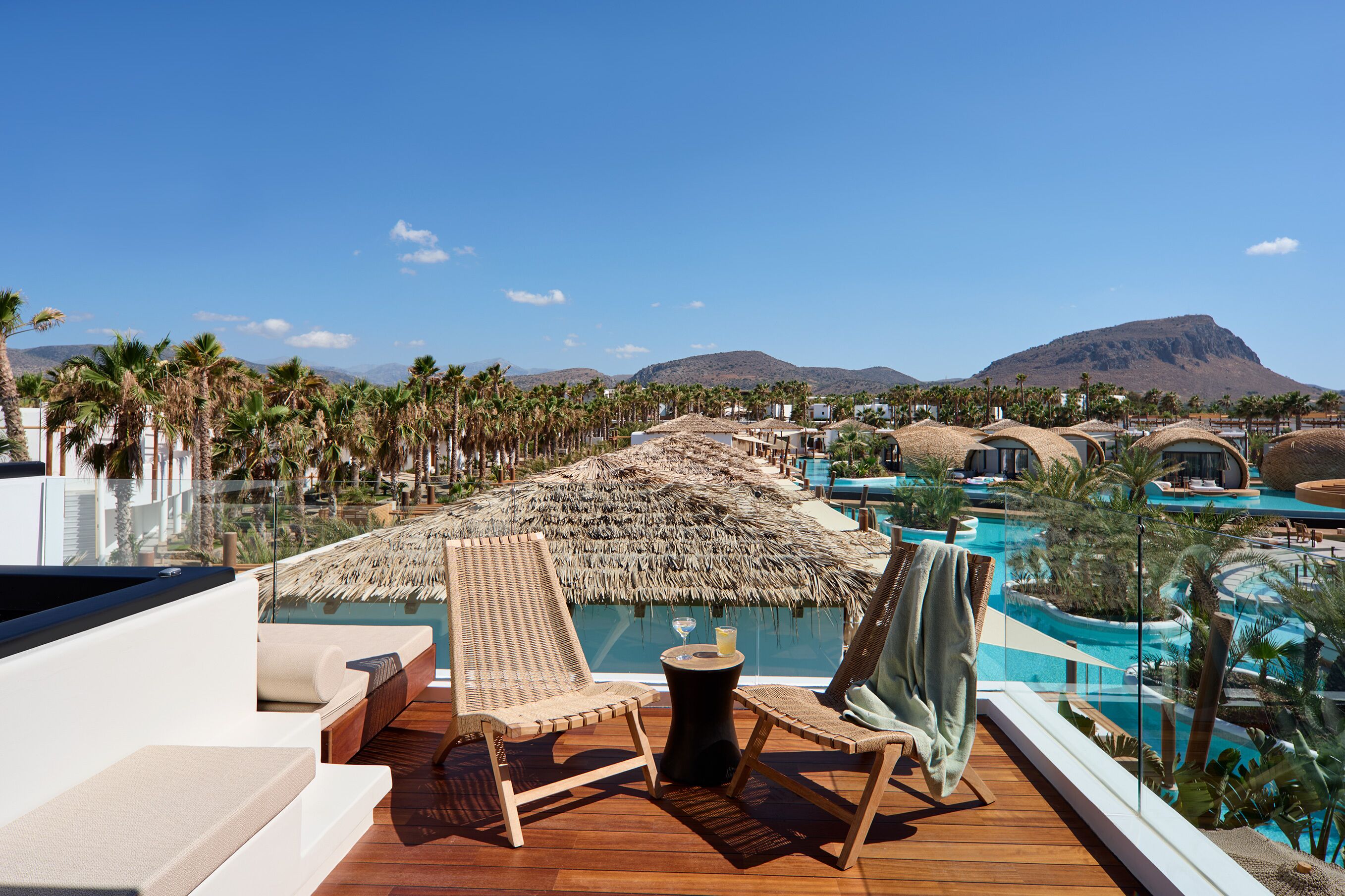 Ein Hotelbalkon mit Holzboden, Liegestühlen, einem Pool und Blick auf die Berge.