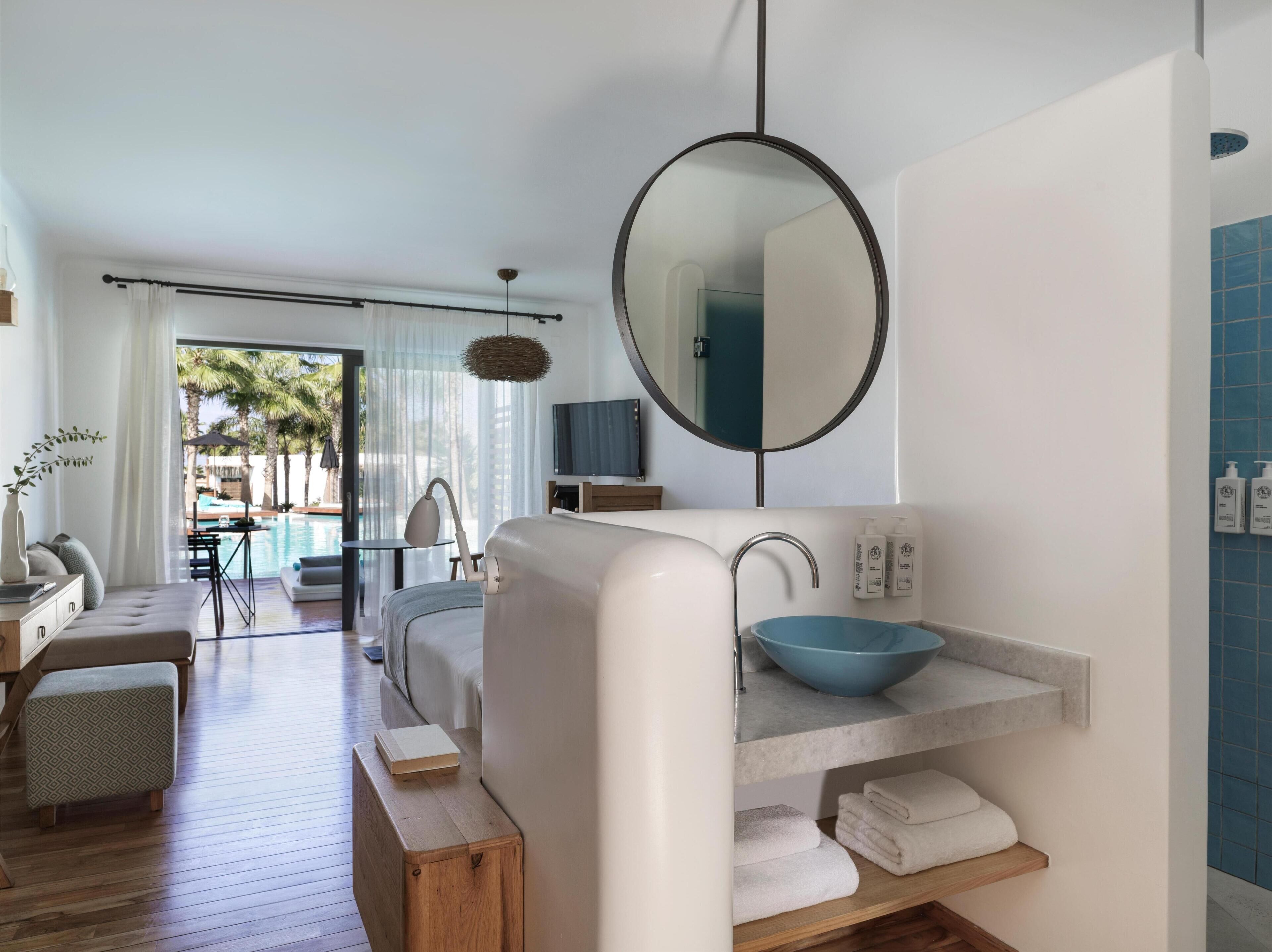 A modern bathroom with a round mirror, a blue basin, and a wooden bench.