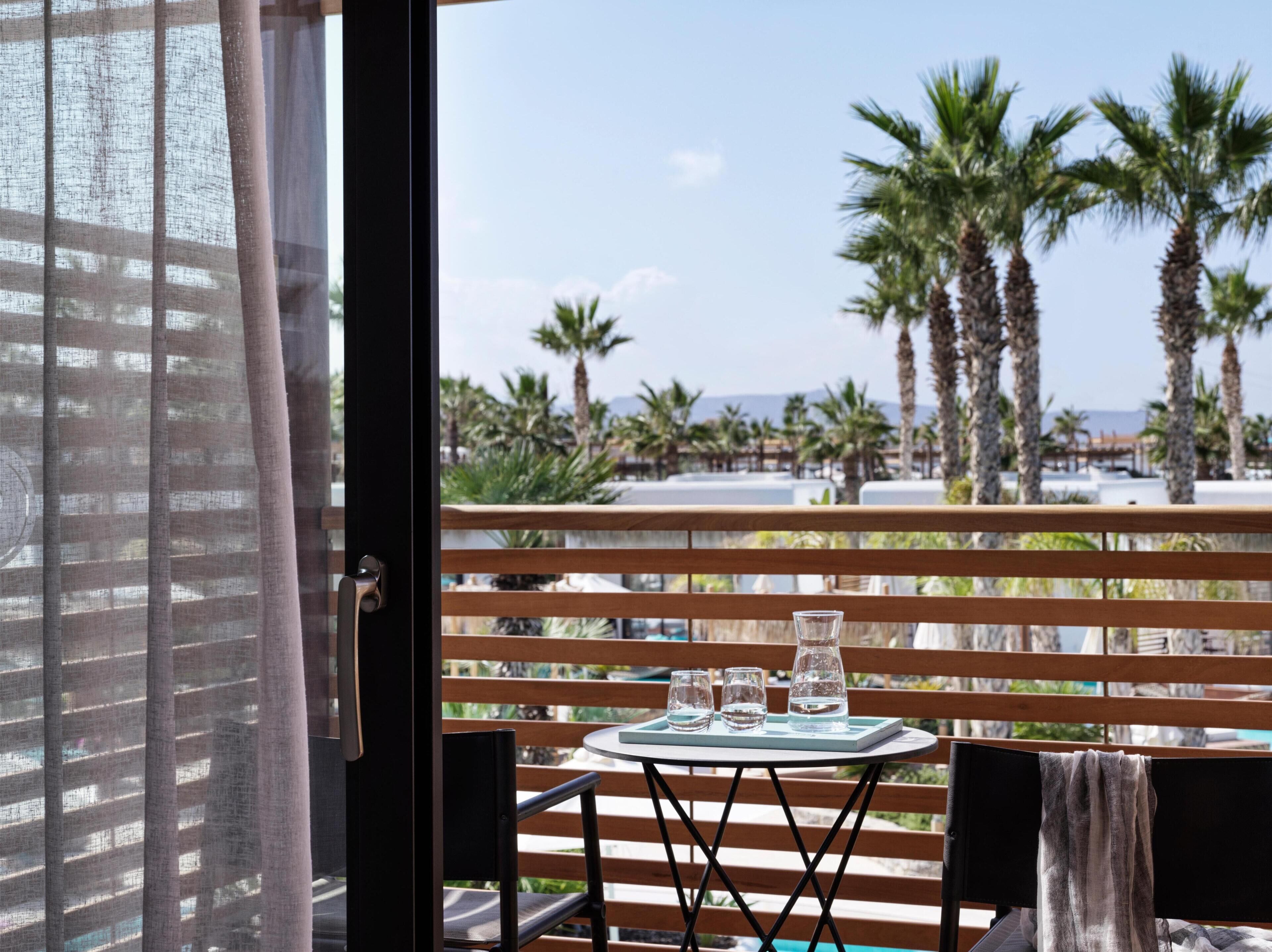 Un balcón con mesa y sillas, con vistas a palmeras y una playa.
