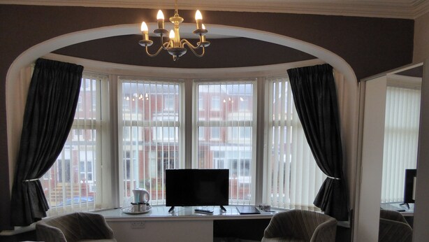 Een hotelkamer met een groot erkerschrijn, een flatscreen-televisie, twee fauteuils, een bureau en een kroonluchter.