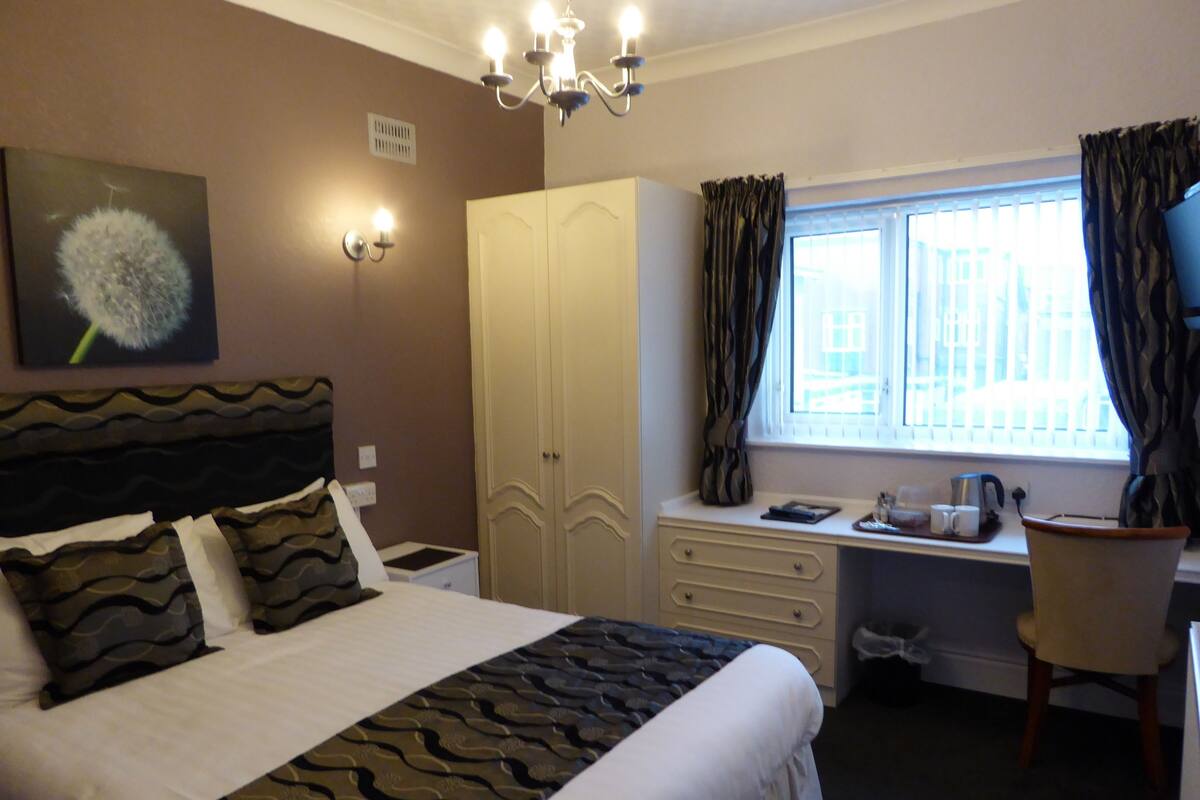 A hotel room with a bed, a desk, a chair, a wardrobe, and a window with curtains.