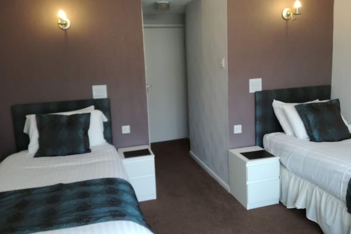 A hotel room with two single beds, white nightstands, and wall-mounted lights.