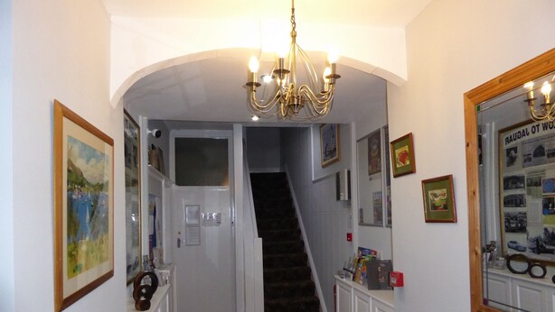 A hallway with a staircase, framed pictures, and a chandelier. - The Berwick - Over 40's Only (Blackpool)
